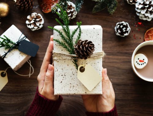 Woman holding Christmas gift on festive table with decorations