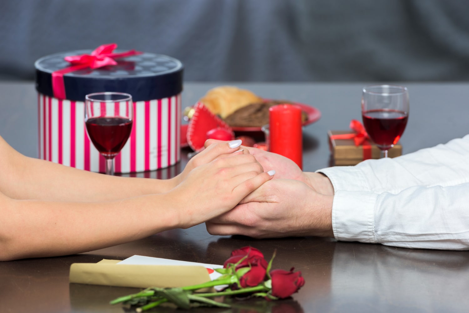 Couple holding hands over dinner with gifts and wine